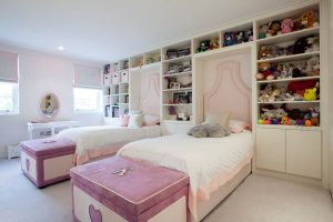 girls pink bedroom with single beds and shelving that extends to the ceiling