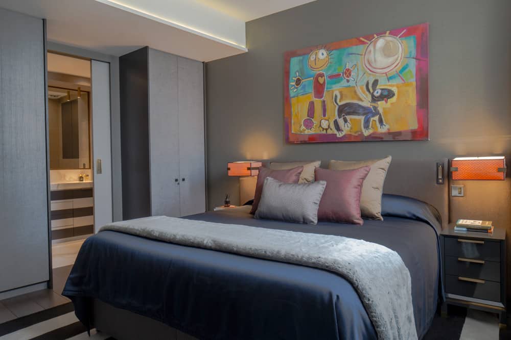 master bedroom with bespoke headboard and lampshades, bright contemporary artwork and striped rug 