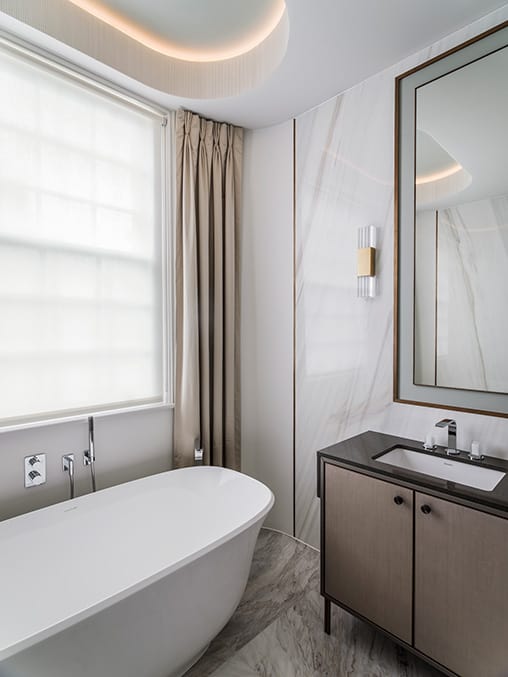 bathroom with large freestanding bath and floor to ceiling curtains on either side of a sash window