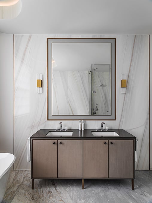 elegant bathroom vanity with brass wall lights on either side of a large bathroom mirror with bronze mirror surround