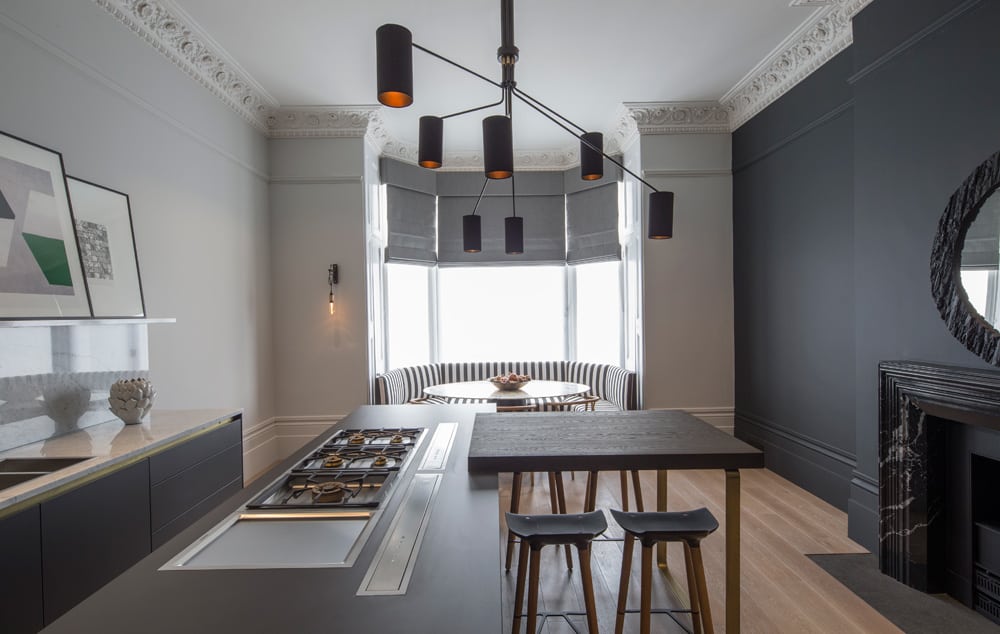 Black and white striped banquette seating in the bay window draws the eye right to the end of this contemporary monochrome kitchen with marble surround fireplace and striking pendant light fixture.