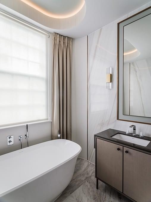 bathroom with large freestanding bath and floor to ceiling curtains on either side of a sash window