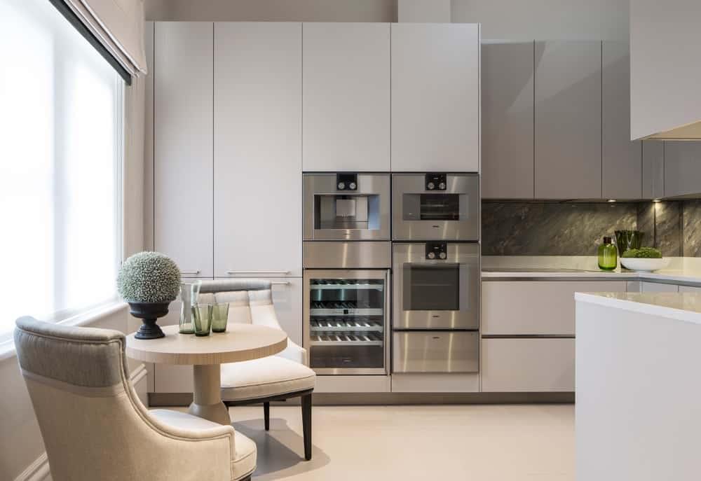 Breakfast Nook - A contemporary white kitchen with elegant window seating consisting of light veneer round table and two upholstered dining chairs by Roselind Wilson Design. 