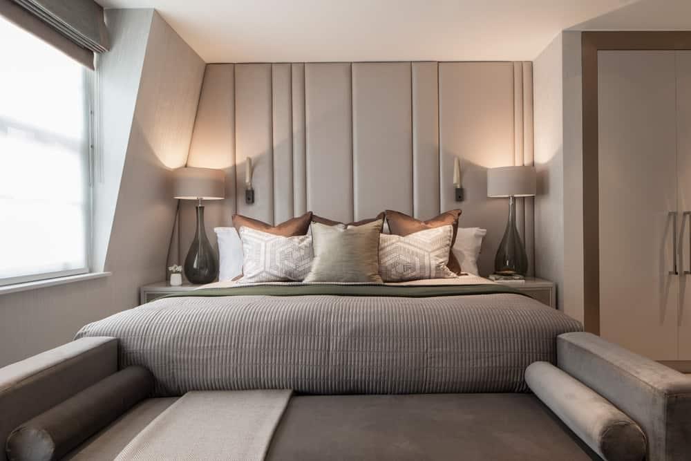 luxury bedroom in a neutral colour palette with ful-height leather headboard and chaise lounge at the foot of the bed by roselind wilson design