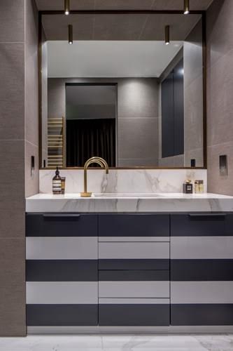 A black and white striped bathroom vanity paired with a Calacatta Oro marble countertop and striking metal framer mirror.