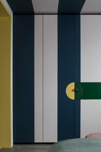 Blue and white vertical stripes on the built-in wardrobe doors contrast with the bright yellow and green of the joinery handle. 