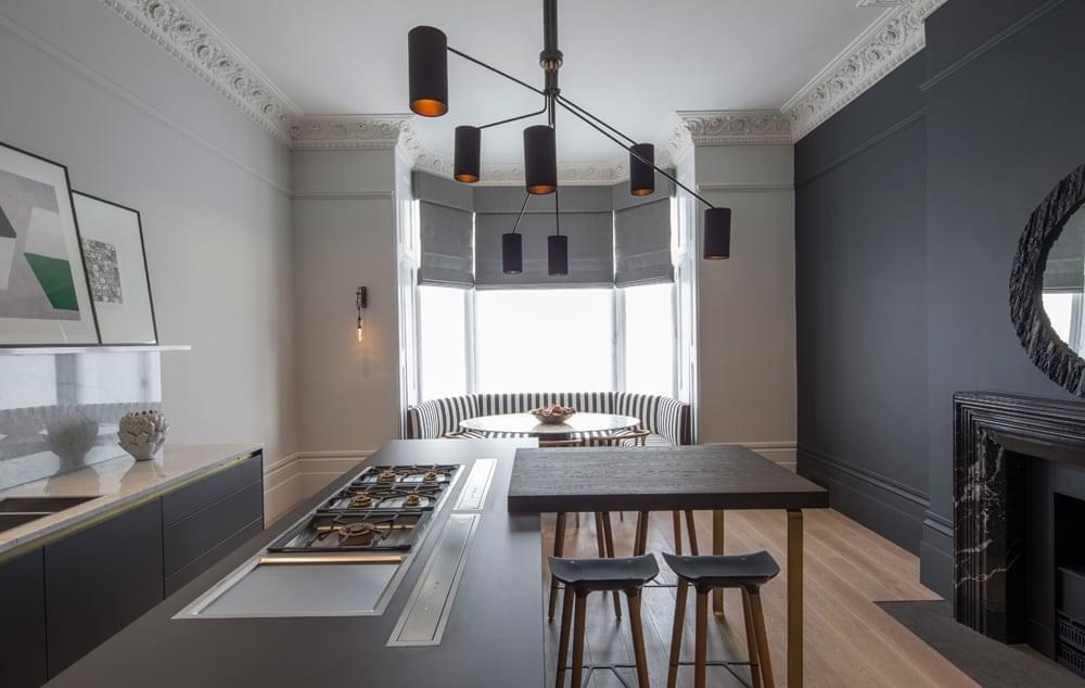 Black and white striped banquette seating in the bay window draws the eye right to the end of this contemporary monochrome kitchen with marble surround fireplace and striking pendant light fixture.